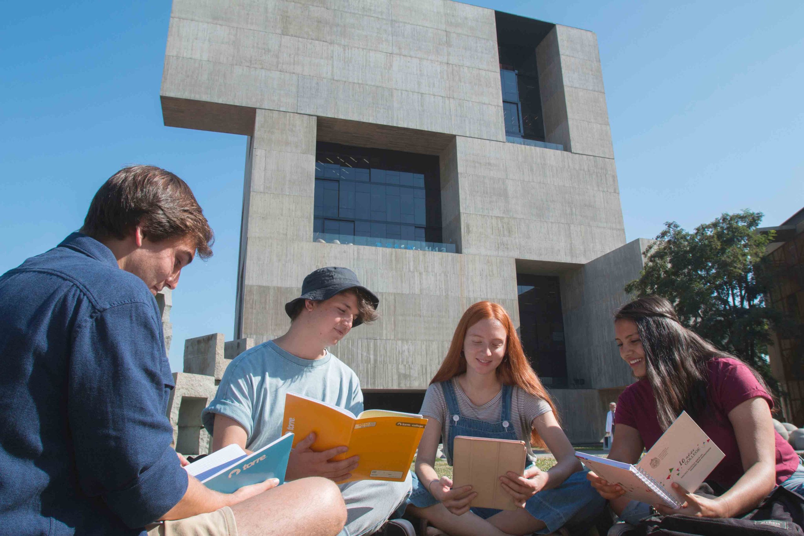 Grupo de estudiantes leyendo libros en el exterior de un edificio moderno.